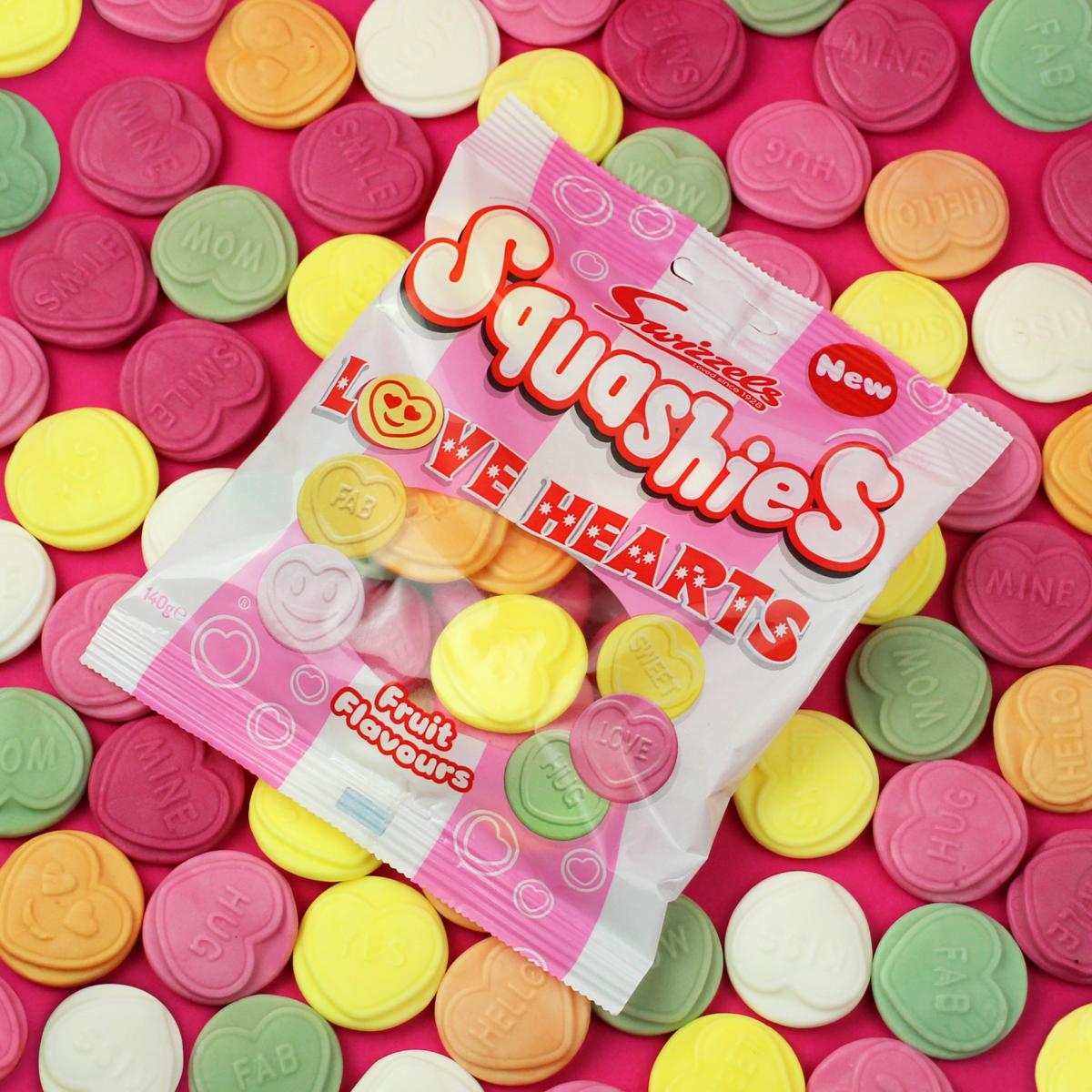 Pack of Squashies Love Hearts candy on a pink background with colorful heart-shaped candies.
