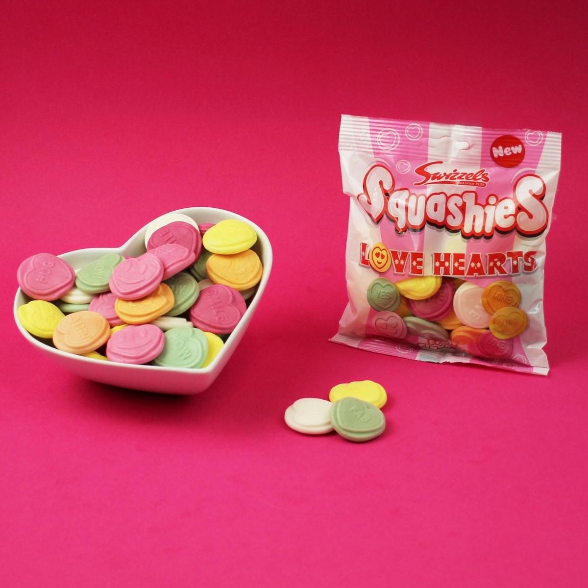 Heart-shaped bowl and package of Swizzles Love Hearts candies on a pink background
