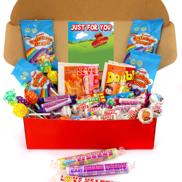 A cardboard gift box filled with assorted colorful candies and lollipops, with three wrapped lollipops placed in front on a white background. The box is lined with branded candy bags including Rainbow Biscuits and Double Toffee.