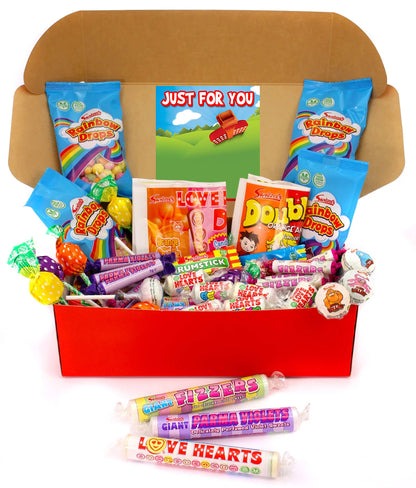 A cardboard gift box filled with assorted colorful candies and lollipops, with three wrapped lollipops placed in front on a white background. The box is lined with branded candy bags including Rainbow Biscuits and Double Toffee.