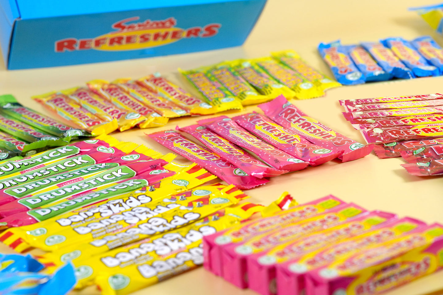 A collection of colorful Snickers Refreshers candy bars and wrappers arranged on a light-colored surface, with a blue box of Snickers Refreshers visible in the background.