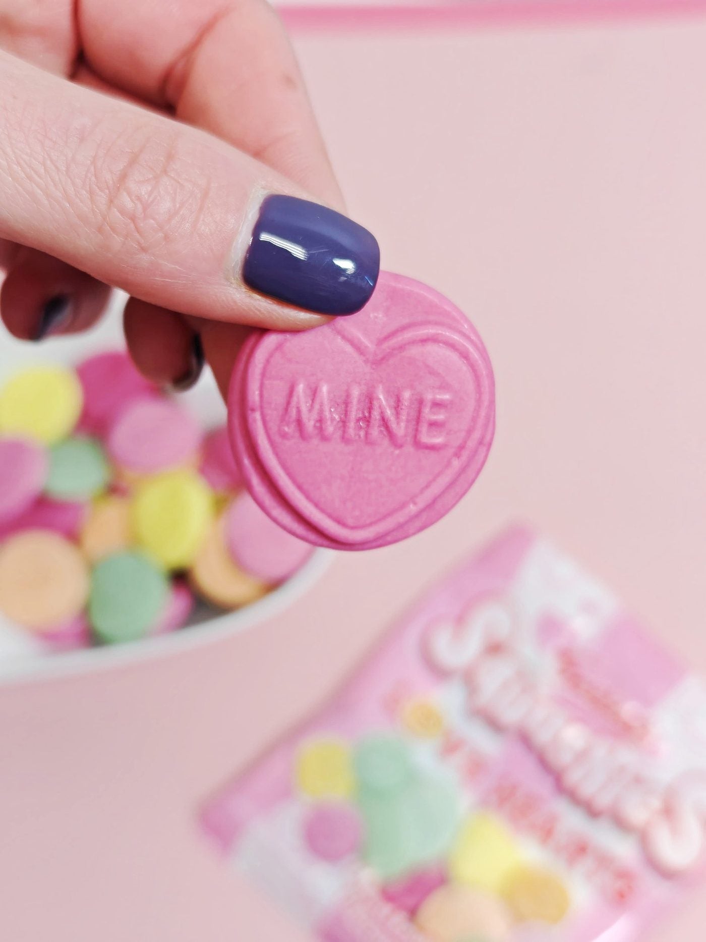 Heart-shaped pink candy with 'LOVE' text held by a hand against a pink background