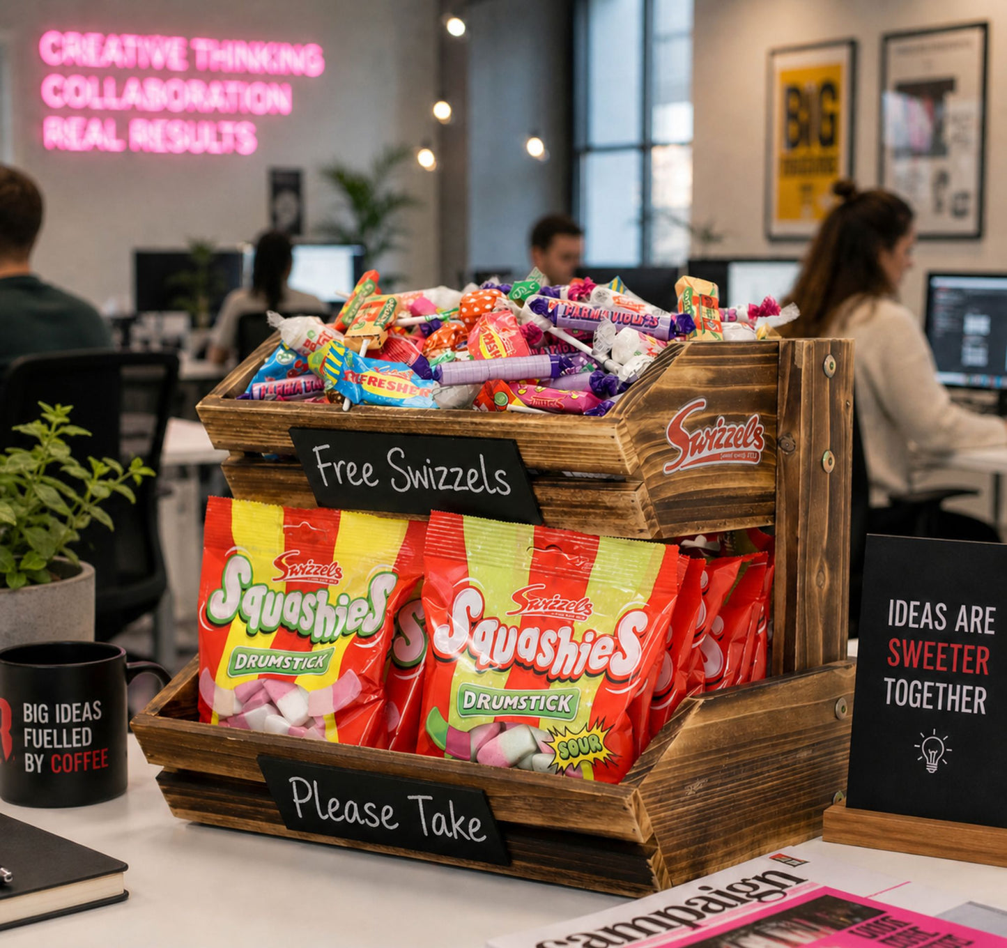 Wooden crate of Swizzles sweets and Squashies on a desk in an office setting with people working in the background.
